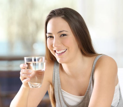Happy woman posing holding a glass of water at home